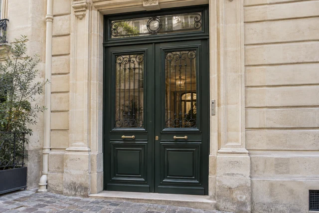 Porte d’immeuble en bois vert foncé et vitrage dans une façade en pierre parisienne
