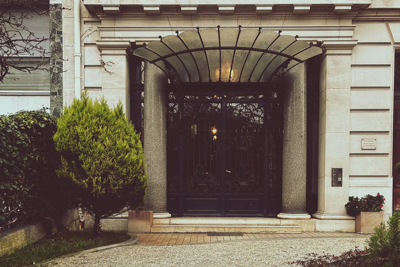 Porte d’entrée en ferronnerie et marquise vitrée sur une façade en pierre